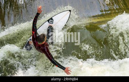 18 août 2023, Bavière, Munich : un surfeur monte sa planche sur la vague de surf Floßlände près de la rivière Isar dans le sud de la capitale bavaroise. Photo : Peter Kneffel/dpa Banque D'Images