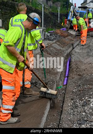 Ouvriers installant des conduits pour câble à fibre optique dans une tranchée coupée sur route avec vibreur compactant le fond de la tranchée avant que le conduit ne soit en place, Royaume-Uni Banque D'Images