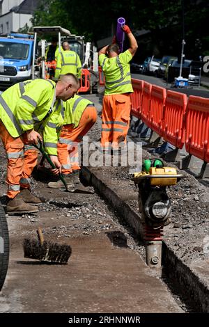 Ouvriers installant des conduits pour câble à fibre optique dans une tranchée coupée sur route avec vibreur compactant le fond de la tranchée avant que le conduit ne soit en place, Royaume-Uni Banque D'Images