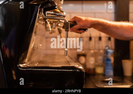 vue rognée de barista floue utilisant la machine à café près de la vapeur et de l'éclairage dans le café Banque D'Images