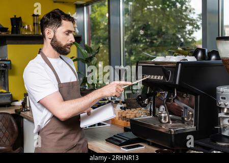 le barista tient son cahier près de la machine à café, du smartphone et de la tablette numérique dans le café Banque D'Images