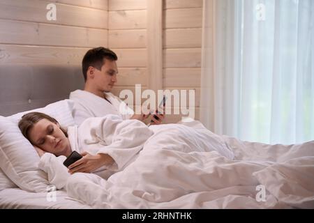 Jeune couple allongé dans son lit et regardant les écrans de smartphones Banque D'Images