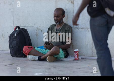 Lisbonne, Portugal - 24 juin 2023 : un homme noir est assis sur la couverture sur le trottoir et regarde son téléphone. Mid shot Banque D'Images