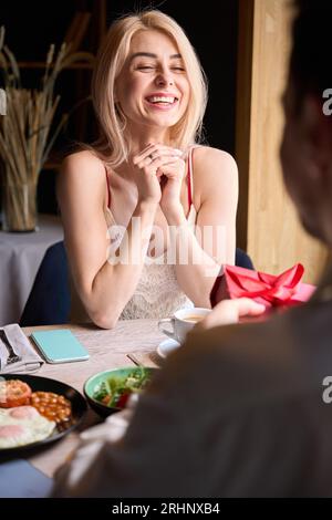 Heureuse femme excitée se réjouissant sincèrement de recevoir le cadeau de l'homme bien-aimé Banque D'Images