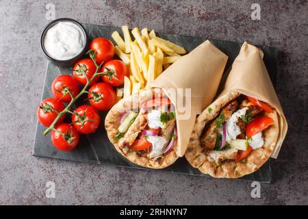 Gyros de poulet avec légumes, frites et sauce tzatziki gros plan sur la planche sur la table. Vue de dessus horizontale Banque D'Images