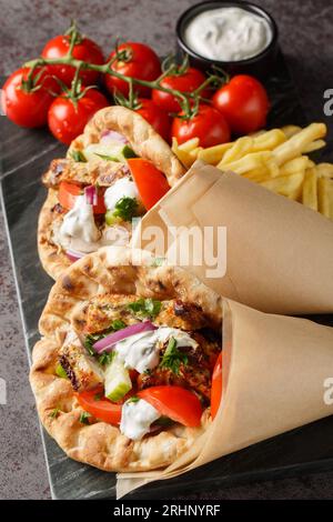 Gyros grecs au poulet et légumes frais servis avec sauce tzatziki et frites en gros plan sur une planche sur la table. Vertical Banque D'Images