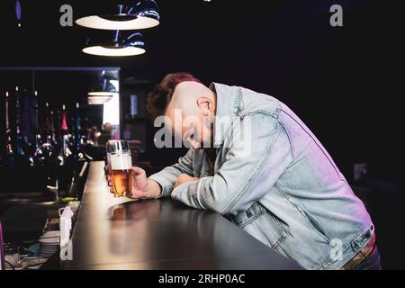 un homme brutal ivre avec un cocktail alcoolisé dans un verre. Le concept des mauvaises habitudes et de la dépendance à l'alcool. Un homme solitaire et triste s'ivre dans un pub irlandais Banque D'Images