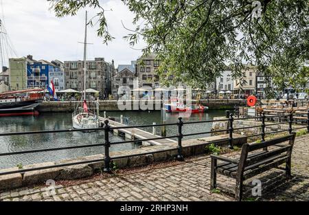 Cafés et bars sur Quay Road à côté du port de Sutton à Plymouth. Au premier plan un siège vacant sous un arbre avec des pavés barbicans. Banque D'Images