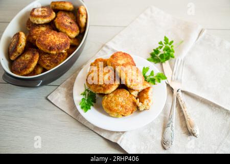 Côtelettes de poisson frites cuites dans une assiette avec des herbes, sur une table en bois clair. Banque D'Images