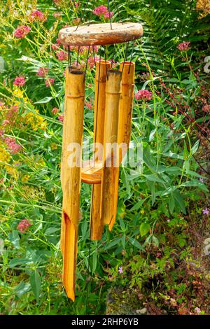 Carillons de vent en bois suspendus à l'extérieur dans un jardin avec des fleurs visibles en arrière-plan. Banque D'Images