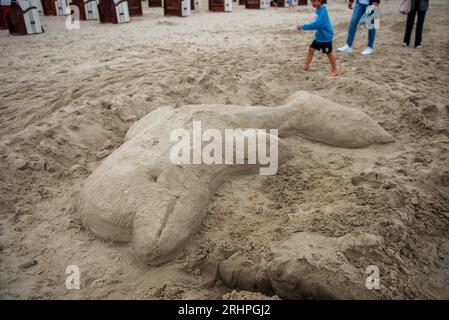 Les gens passent devant une sculpture de sable d'un dauphin sur la plage Banque D'Images