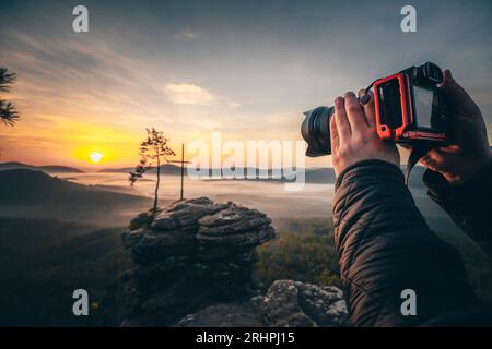 Sommet croix et point de vue, le Rötzenfels dans la forêt du Palatinat, lever de soleil au printemps dans un paysage brumeux, photographe avec appareil photo, détail Banque D'Images