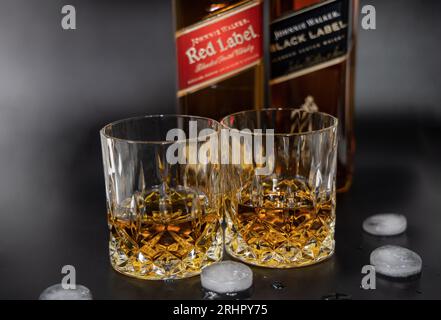 Deux verres de whisky sur le fond d'une bouteille de Johnnie Walker Wiskey, Red Label et Black Label. Banque D'Images