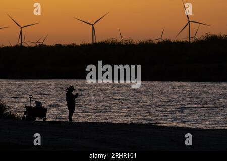 Un pêcheur solitaire se tient près du bord de l'eau joliment silhouetté contre un ciel de coucher de soleil brillant dans le sud du Texas. Banque D'Images