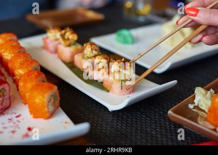 Une main de femme prend des rouleaux de poisson japonais. Banque D'Images
