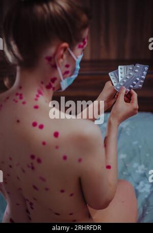 Une jeune femme atteinte de varicelle portant un masque médical choisit des pilules Banque D'Images