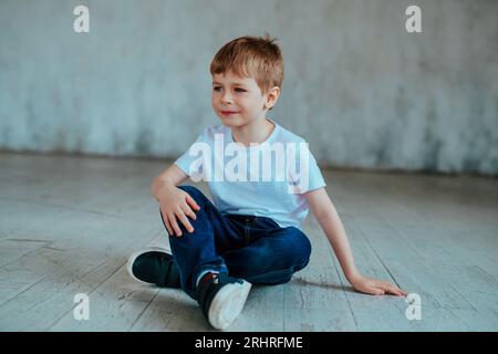 Mignon garçon de cinq ans dans un t-shirt et un Jean est assis sur le sol Banque D'Images