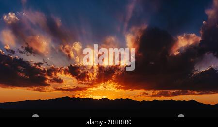 Ciel dramatique rouge coloré à la lumière du coucher du soleil avec silhouettes de montagnes Banque D'Images