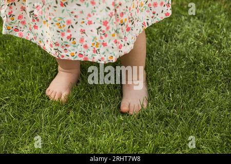 Petite fille apprenant à marcher sur l'herbe verte à l'extérieur, gros plan Banque D'Images