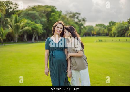 Un moment réconfortant capturé dans le parc comme une femme enceinte après 40 partage un lien spécial avec sa fille adolescente, embrassant la beauté de Banque D'Images