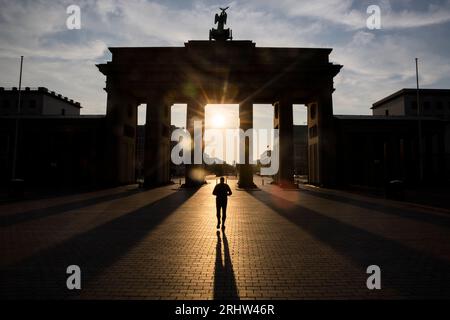Berlin, Allemagne. 19 août 2023. Un homme traverse la porte de Brandebourg alors que le soleil se lève. Les gens à Berlin et Brandebourg doivent se préparer à une chaleur forte à extrême samedi. Crédit : Christoph Soeder/dpa/Alamy Live News Banque D'Images
