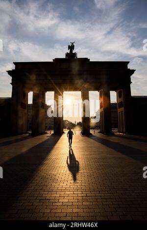 Berlin, Allemagne. 19 août 2023. Un homme traverse la porte de Brandebourg alors que le soleil se lève. Les gens à Berlin et Brandebourg doivent se préparer à une chaleur forte à extrême samedi. Crédit : Christoph Soeder/dpa/Alamy Live News Banque D'Images