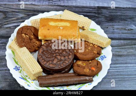 Une assiette de bonbons avec des bâtonnets de chocolat, des gaufrettes croquantes avec garniture à la crème au chocolat, des biscuits croquants garnis de vanille, du gâteau roulé suisse garni Banque D'Images