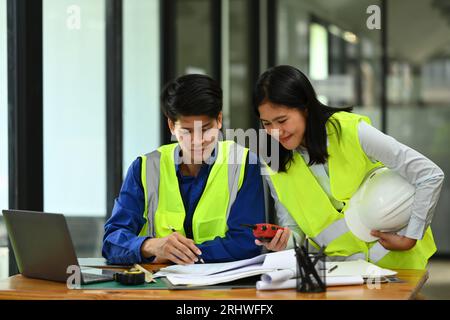 Ingénieurs homme et femme portant des gilets jaunes travaillant avec Blueprint, discutant du nouveau projet au bureau Banque D'Images