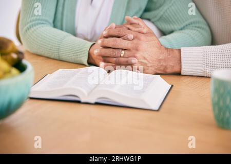 Lecture, bible et couple senior se tenant la main à la maison avec l'étude du livre et la religion ensemble. Prière, soutien et personnes âgées avec culte Banque D'Images