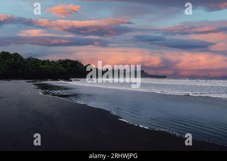 Plage de sable volcanique avec vagues océaniques à Bali. Côte de sable noir et coucher de soleil ou lever du soleil ciel nuageux Banque D'Images