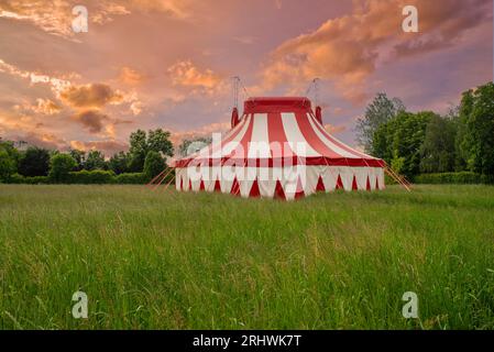 Tente de cirque colorée sur un pré vert contre un ciel de coucher de soleil coloré Banque D'Images