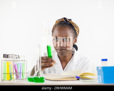 Jeune femme scientifique observant vivement un échantillon liquide tenu cylindre de mesure alors qu'il se trouvait dans un laboratoire Banque D'Images