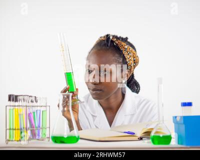 Jeune femme scientifique observant vivement un échantillon liquide tenu cylindre de mesure alors qu'il se trouvait dans un laboratoire Banque D'Images