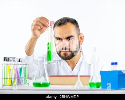 Jeune homme scientifique observant vivement un échantillon liquide tenu cylindre de mesure pendant qu'il se trouvait dans un laboratoire Banque D'Images