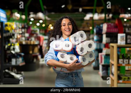 Heureuse femme shopper souriant a acheté beaucoup de rouleaux de papier toilette dans le supermarché. Banque D'Images