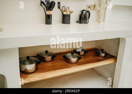 pots en acier inoxydable avec couvercles en verre sur étagère en bois. Trucs de cuisine et bouilloire. Design moderne blanc lumineux de la cuisine de luxe Banque D'Images