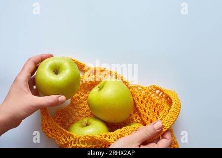 Une main femelle place les pommes dans un sac à cordes jaune. Le concept de rejet du plastique et du polyéthylène. Concept zéro déchet, vue de dessus. Banque D'Images