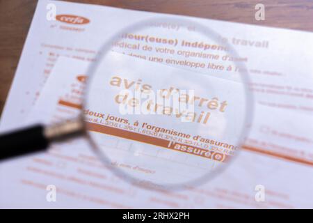 France : gros plan à travers une loupe d'un formulaire officiel de congé de maladie ('Avis d'arrêt de travail') de la sécurité sociale française Banque D'Images