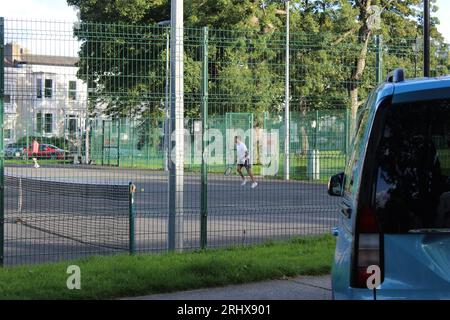 Photo d'une personne jouant au tennis sur un court de tennis clôturé en béton Banque D'Images