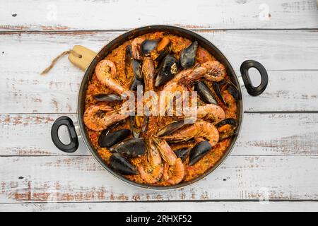 Vue de dessus de la paella espagnole fraîchement cuite à base de riz et de fruits de mer servi dans une casserole sur une table en bois dans la cuisine Banque D'Images