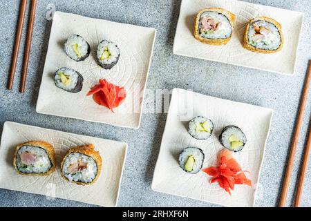 D'en haut de divers rouleaux de sushi placés sur des assiettes avec des baguettes et de la sauce soja sur fond blanc Banque D'Images