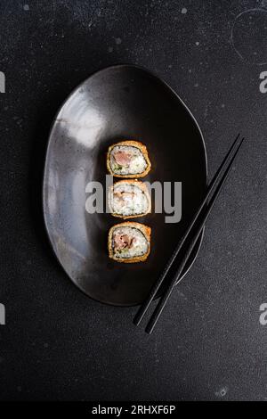 De la rangée ci-dessus de savoureux rouleaux de sushi frits avec du riz cuit et du saumon avec des tranches d'avocat sur une plaque noire en céramique sur la table Banque D'Images
