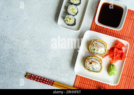 D'en haut de divers rouleaux de sushi placés sur des assiettes avec des baguettes et de la sauce soja sur fond blanc Banque D'Images