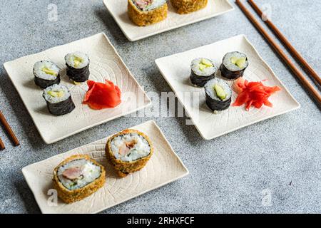 Divers rouleaux de sushi placés sur des assiettes avec des baguettes et de la sauce soja sur fond blanc Banque D'Images