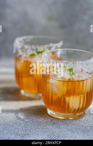 Verres avec liqueur de sochu japonais avec du jus de mangue et des tranches de poivre de Jalapeno avec du sel sur le bord du verre placé sur fond gris Banque D'Images