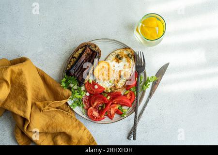 Du haut de l'assiette avec délicieux déjeuner sain, y compris des œufs au plat avec des tranches de tomates, du persil, de l'oignon de printemps, des câpres servies avec un verre de pu froid Banque D'Images