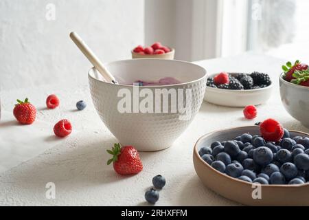 Bol avec du yaourt naturel et quelques fruits frais à l'intérieur : framboises, bleuets, fraises et mûres près des assiettes avec des fruits frais en daylig Banque D'Images