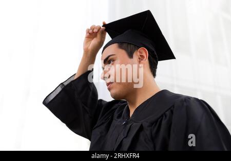 De ci-dessous portrait d'un bel homme confiant portant une robe de graduation noire et une casquette debout regardant loin Banque D'Images