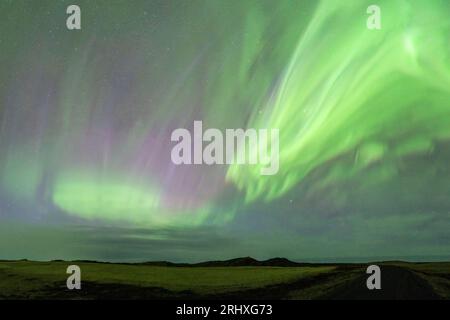 Paysage spectaculaire de lumières vertes du Nord illuminant le ciel sombre sur prairie verte et montagne Banque D'Images