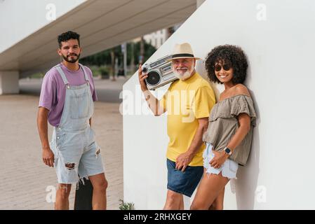 Amis multiethniques positifs dans des vêtements décontractés avec skateboard et stéréo debout sur la rue de la ville et passer du temps ensemble Banque D'Images